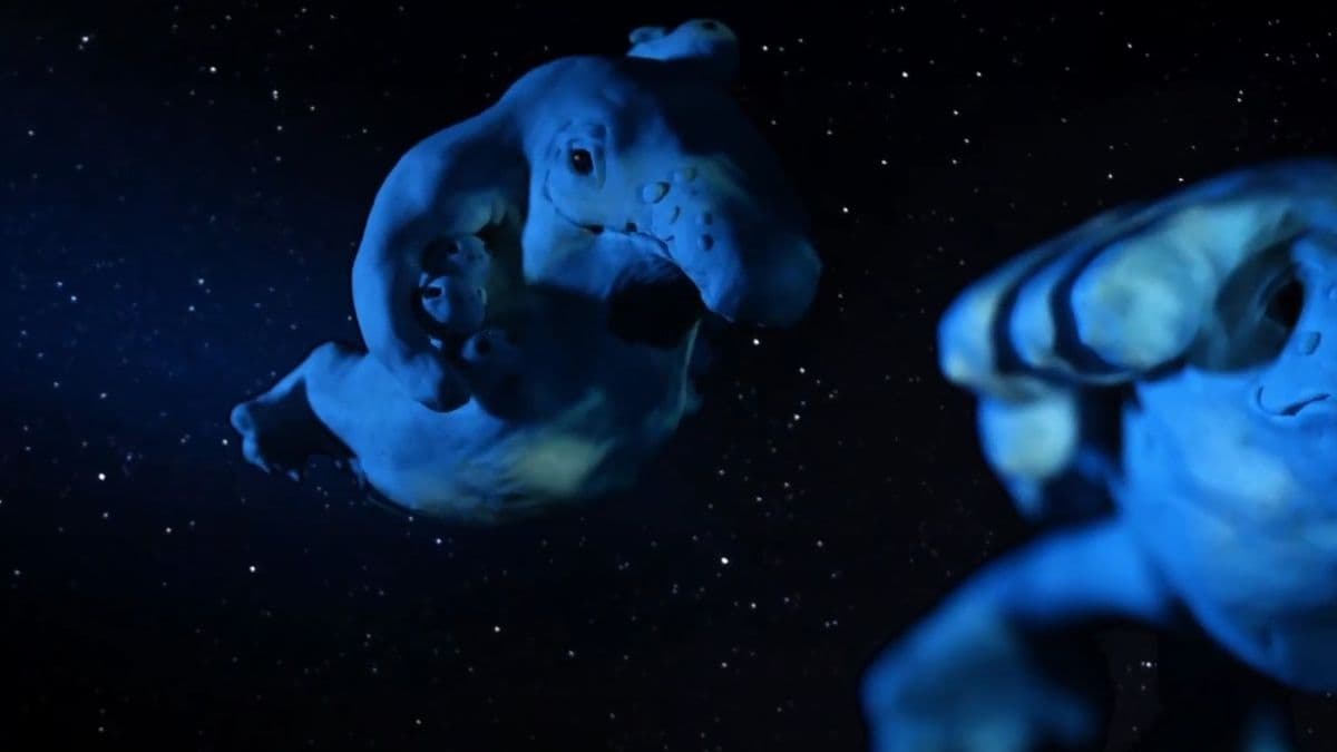a screenshot of a music video still showing two claymation 'skywhale' sculptures suspended against a starry sky