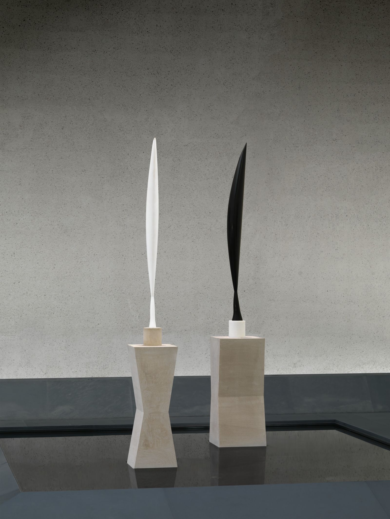 Photo image of two curved and slim abstract sculptures, one in black and one in white