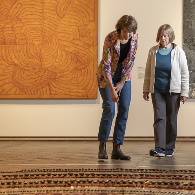 Photograph of two women standing and pointing at artwork on the ground.